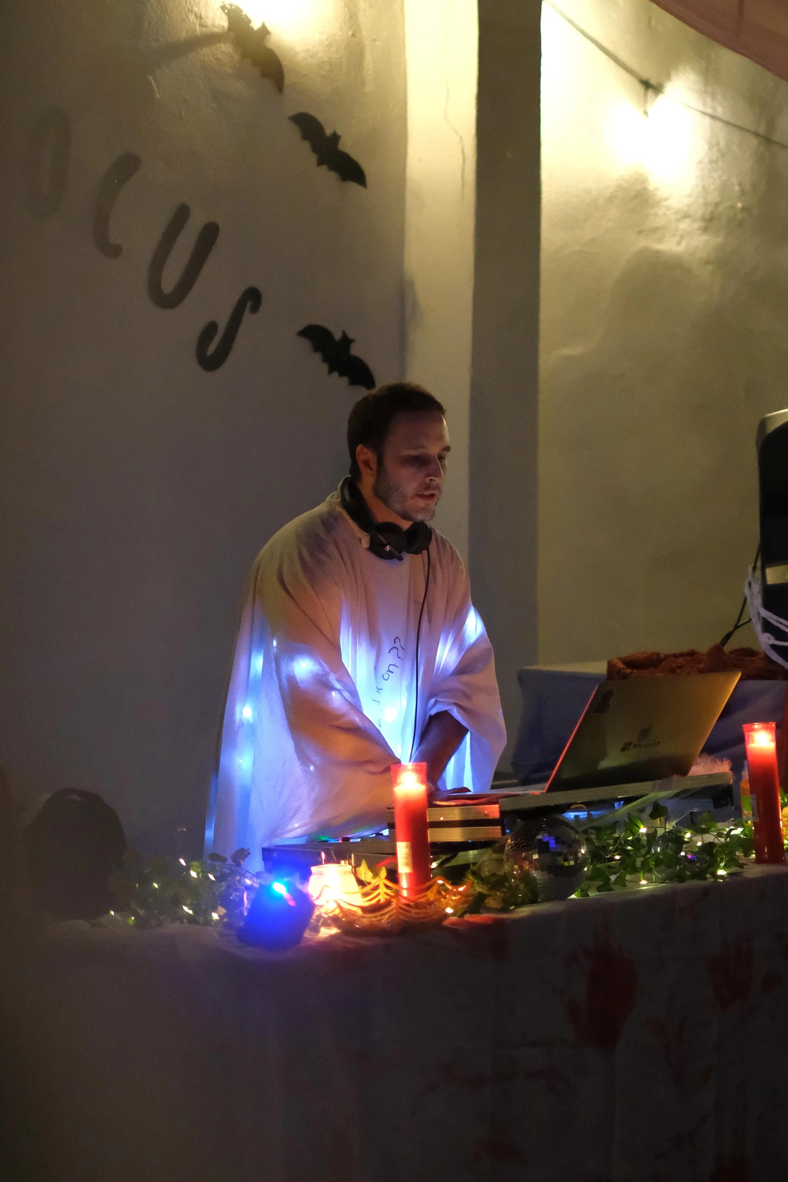 A DJ plays behind a candlelit table decorated with lights and cobwebs.
