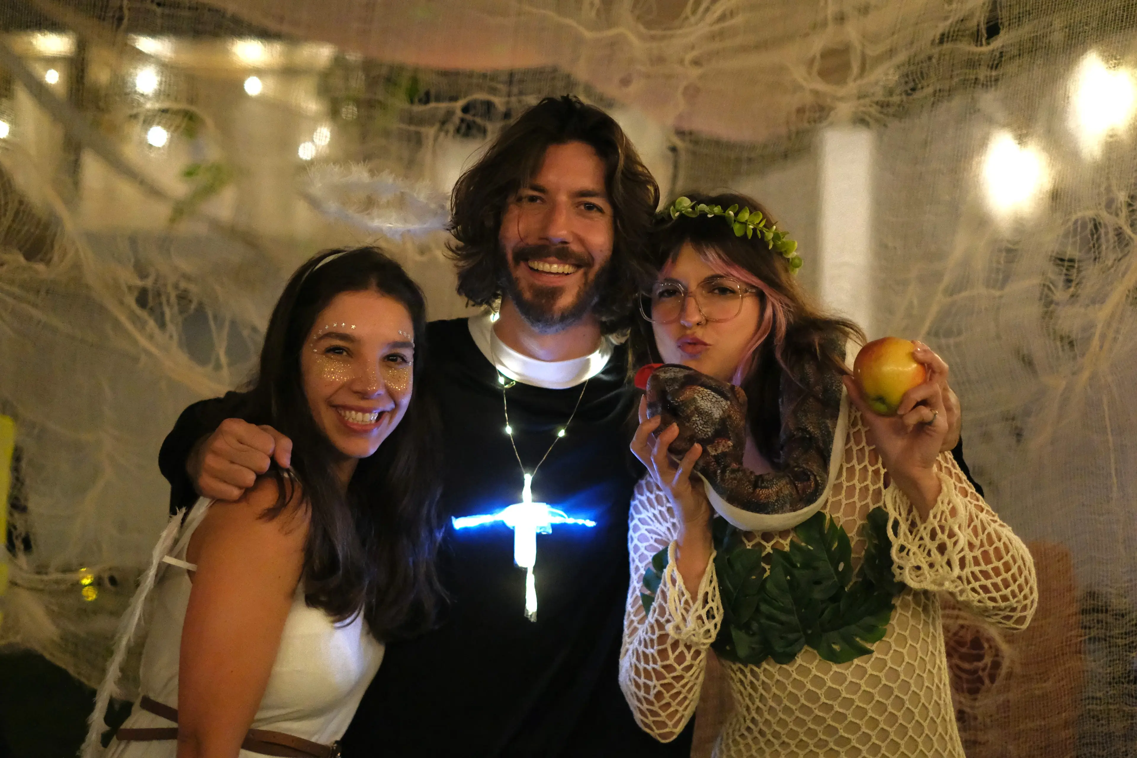 Three friends in angel, priest and ivy costumes pose together.