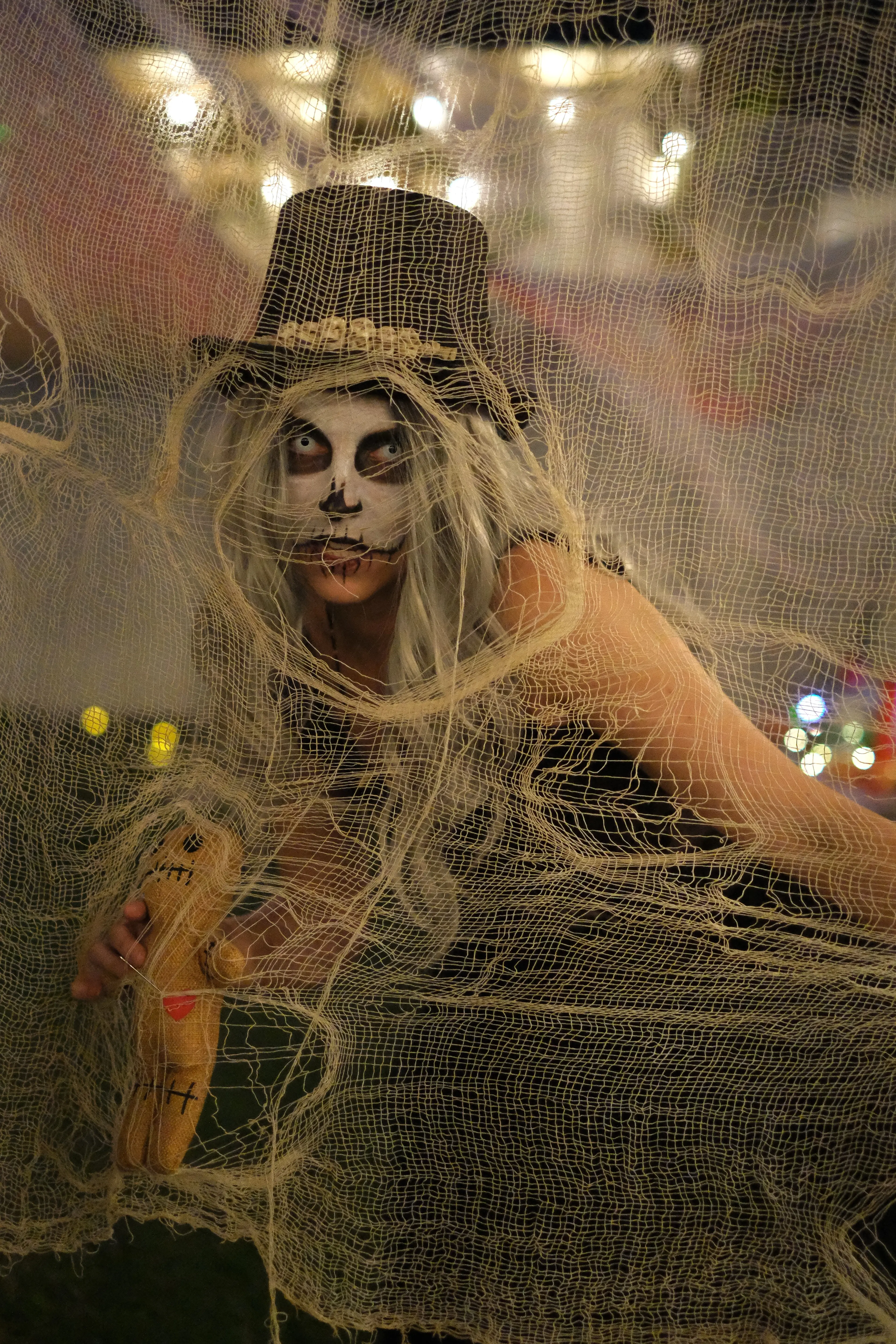 A guest with skull makeup and a tall black hat peers through gauze.